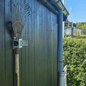 Et redskabsophæng i metal på en sort trævæg der holder 1 redskab med hovedet opad. Ophænget har en holder til et redskab.