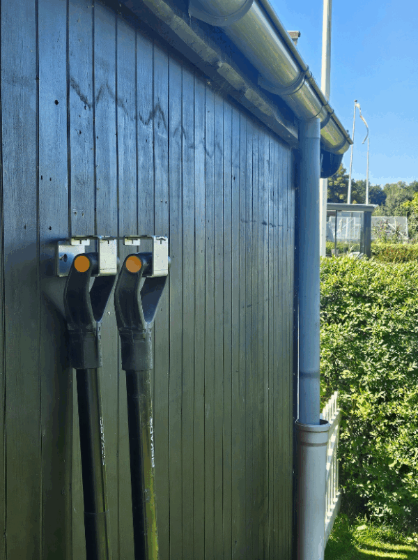 Viting-redskabsophæng-2-2 Et redskabsophæng i metal på en sort trævæg der holder 2 redskaber i deres greb. Ophænget har individuelle holdere til hvert redskab hvor den ene holder er åbnet.