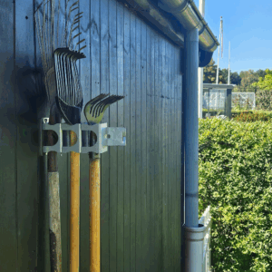 det robuste redskabsophæng i metal på en sort trævæg der holder 3 redskaber med deres hoved opad. Ophænget har individuelle holdere til hvert redskab.