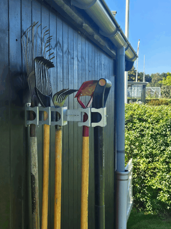 Viting-redskabsophæng-5-4 Et redskabsophæng i metal på en sort trævæg der holder 5 redskaber opad. Ophænget har individuelle holdere til hvert redskab, hvor den ene af holderne er åbnet.