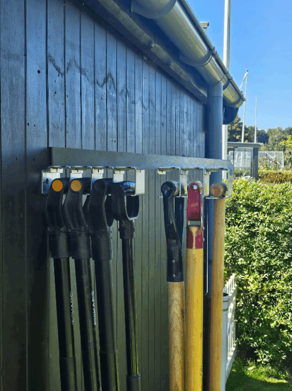 Viting-redskabsophæng-7-2 Et redskabsophæng i metal på en sort trævæg der holder 7 redskaber i deres greb. Ophænget har individuelle holdere til hvert redskab hvor den ene holder er åben.