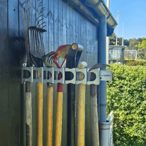 Et smart haveredskabsophæng i metal på en sort trævæg der holder 7 redskaber med hovedet opad. Ophænget har individuelle holdere til hvert redskab. Denne kan holde op til 7 haveredskaber